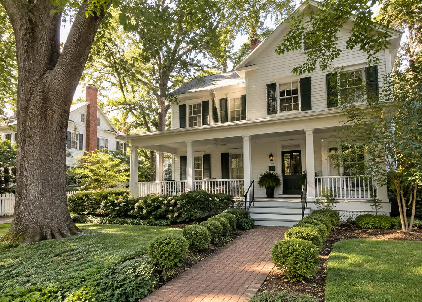 White farmhouse-style home with green shutters and a front porch on a tree-lined Virginia street